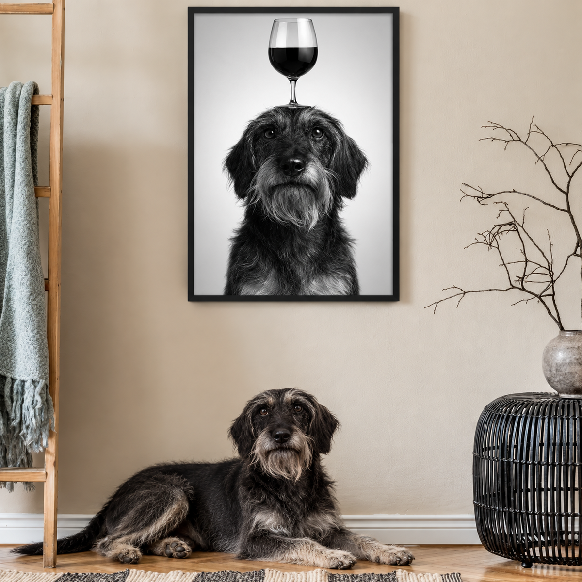 Black-and-white poster of a dog with a wine glass on its head, hanging on the wall. A dog lying on the floor in front.