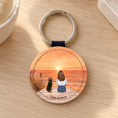 Personalized round keychain with an illustration of a woman and a dog at sunset.