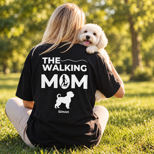 Black personalized T-shirt printed with "THE WALKING MOM" and dog motif. Wearer sitting outdoors.
