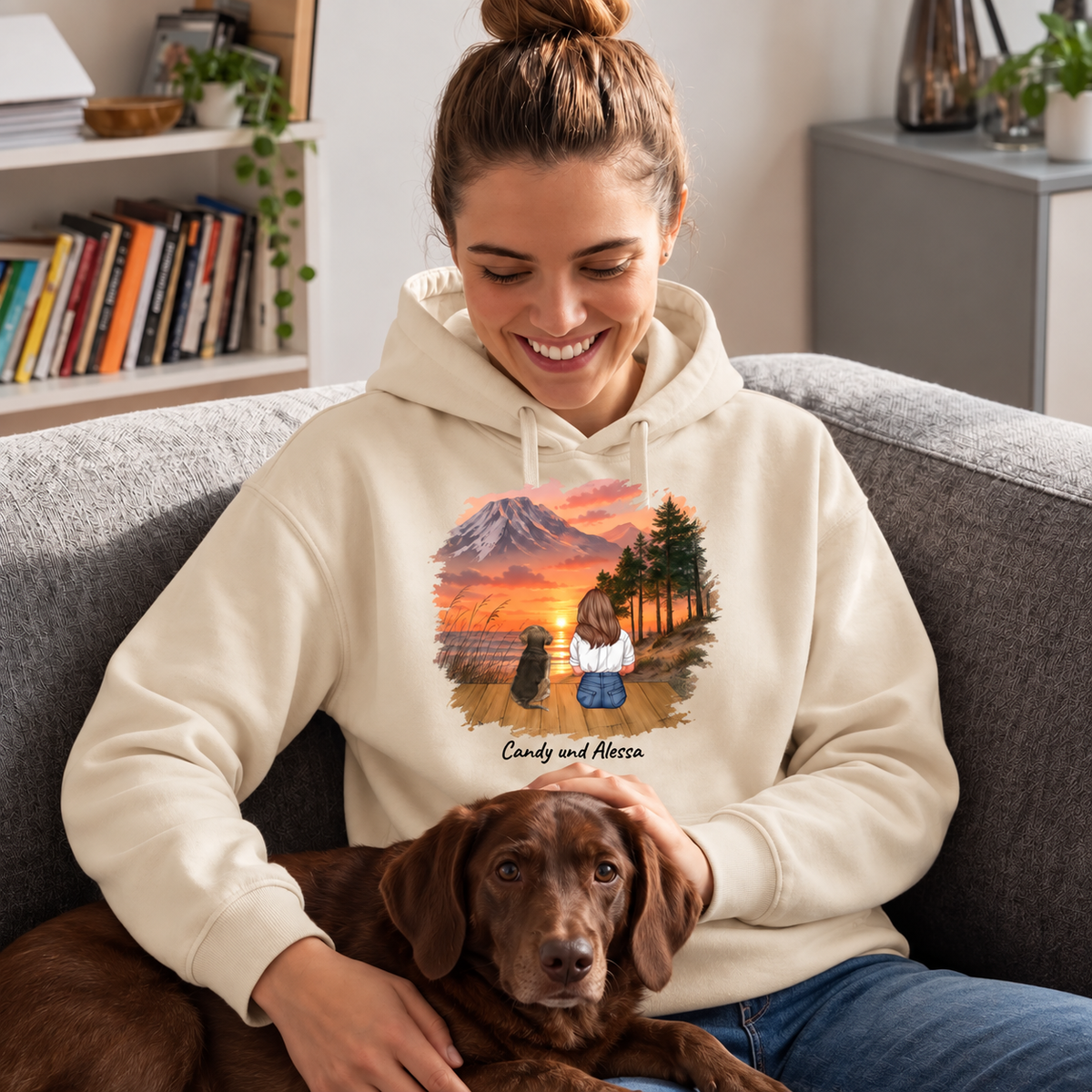 Beige hoodie with personalized print of a woman and dog against a sunset, sitting on a sofa with a dog.