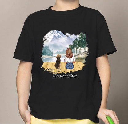 Black kids' T-shirt with a graphic of a girl and dog by a lake with mountains in the background.