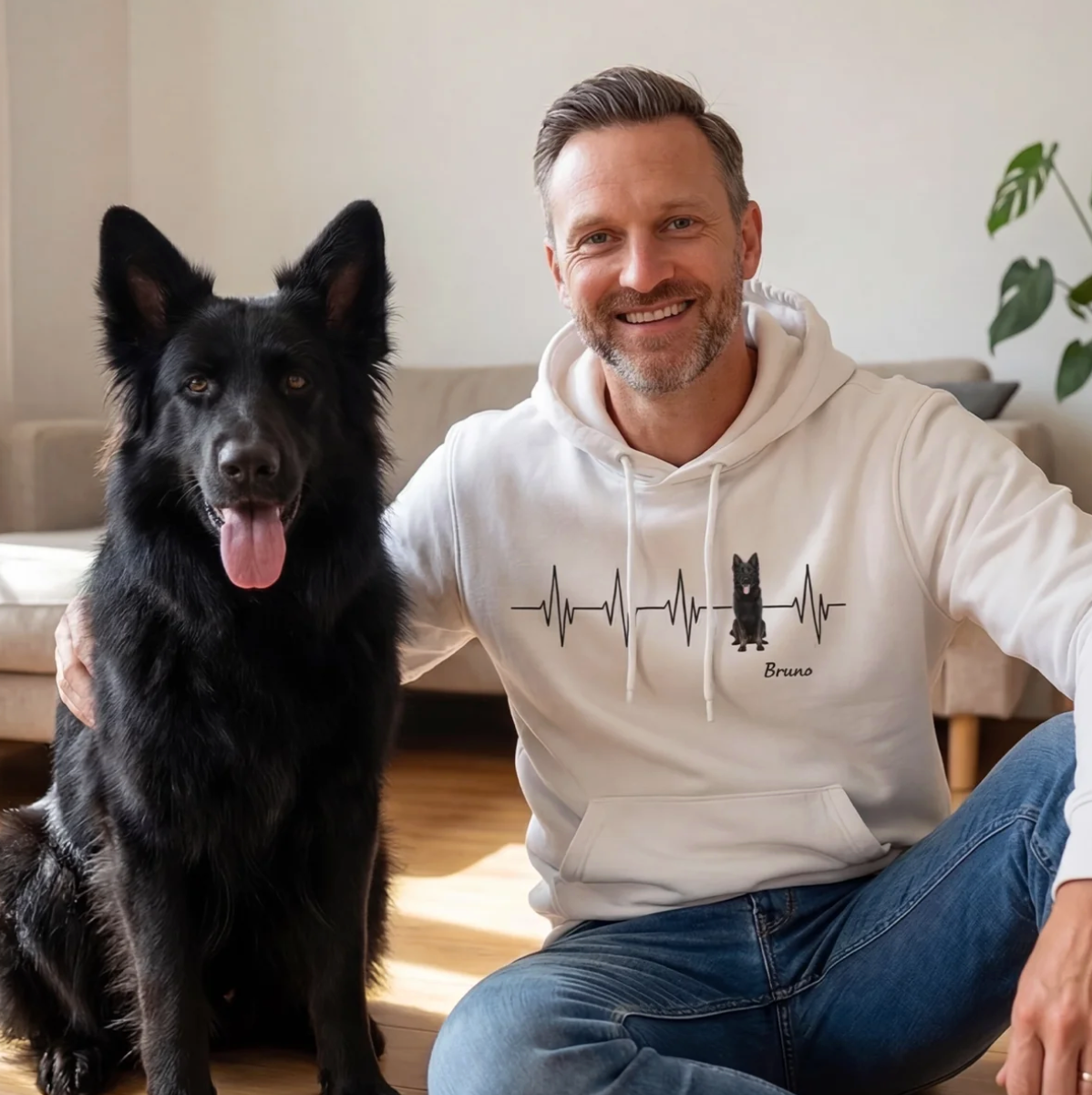 White hoodie with heartbeat pattern and dog motif, man sitting next to a black dog.