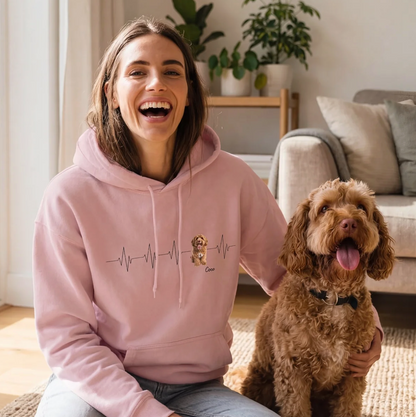Person wearing a pink hoodie with heartbeat design, sitting on a rug next to a dog.