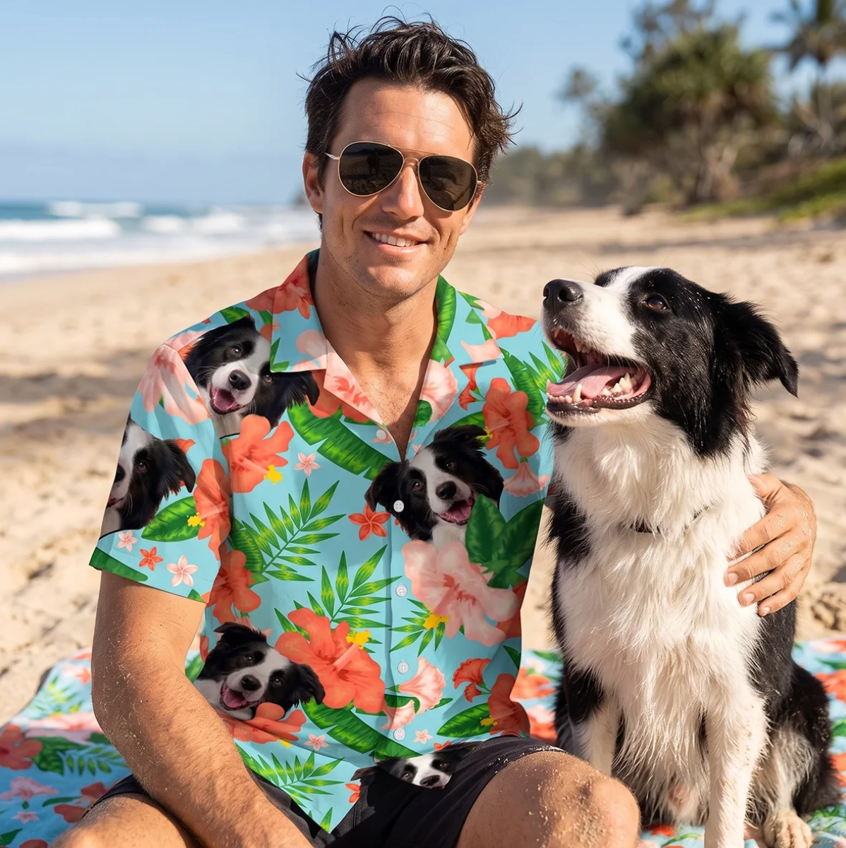 Man in sunglasses wearing a personalized Hawaiian shirt with dog designs, sitting on the beach next to a dog.