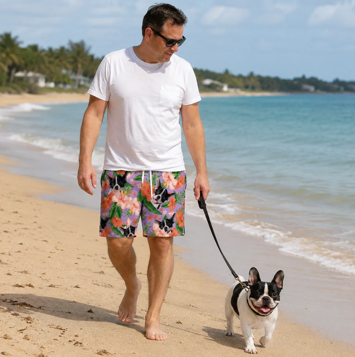 Man wearing personalized swim shorts with colourful flower and animal pattern, walking barefoot on the beach.