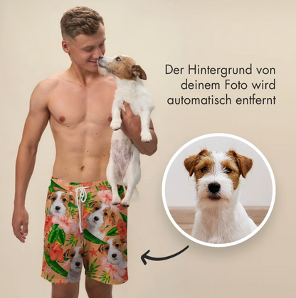 Man in short swim shorts printed with dog and flower design, holding a dog in his arms.
