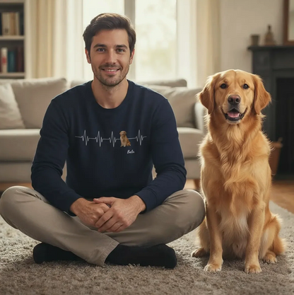 Man sitting on the rug in the living room wearing a black sweatshirt with heartbeat design, a golden retriever next to him.