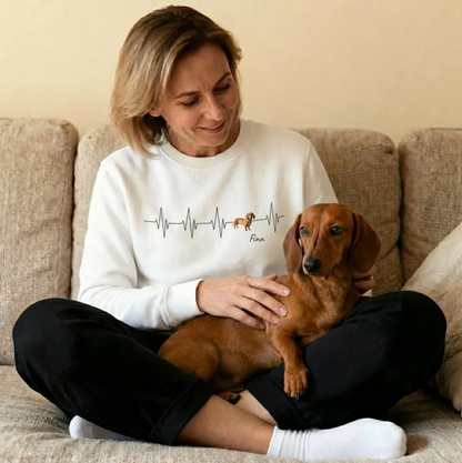 White sweatshirt with heartbeat design and a dog, smiling woman sitting on a sofa with a dachshund.