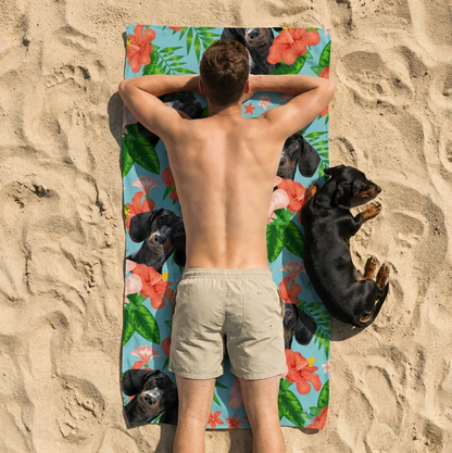 Person lying on a personalized beach towel with dog designs, surrounded by sand.
