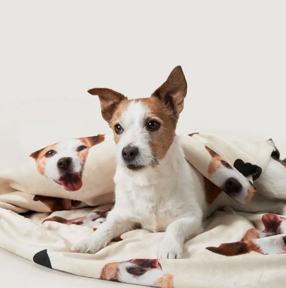 Personalized blanket with dog pictures, cream background and soft material. Dog lying on it.