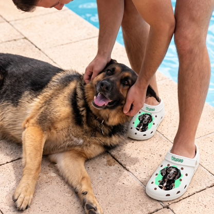 Person wearing personalized white clogs with pet portrait, sitting next to a dog by the water.